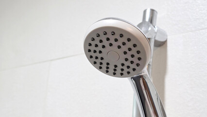 Close-up of a modern handheld shower head with a chrome finish, mounted on a bathroom wall with light-colored textured tiles