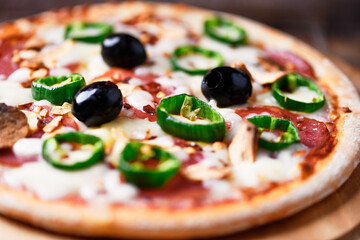 Pizza with salami and mozzarella cheese, jalapeno pepper and black olives. Wooden background. Soft focus. Close up.