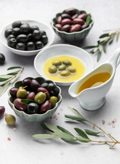 Bowls of various olives with olive oil and olive branches on marble table