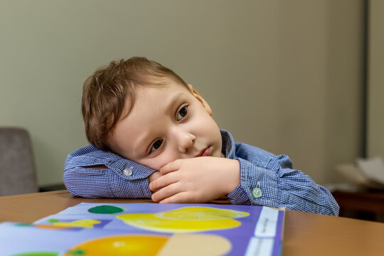 Thoughtful young boy resting head on arms, looking away in contemplation at desk.