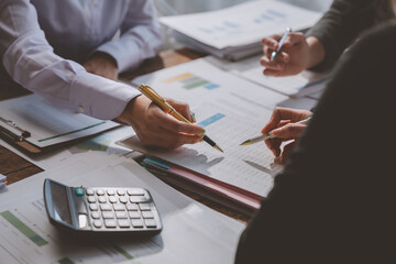 Business team members are reviewing financial reports, pointing at charts and discussing data with...