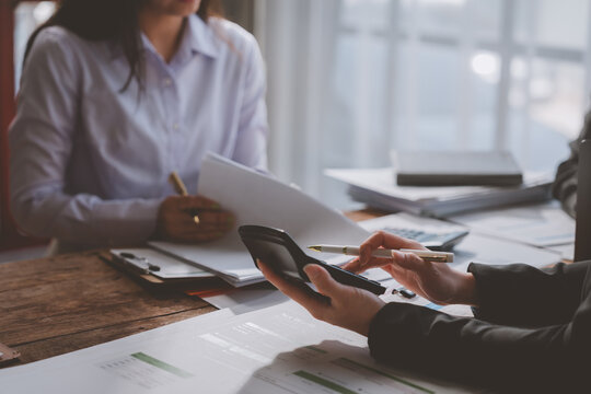 Businesswomen are using a calculator and reviewing documents at a wooden table in the office, collaborating on financial analysis and accounting tasks