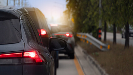 Rear side of cars on the road with turn on brake light. Background is blurred suggesting movement and depth with glimpses of red tail lights and sunlight filtering through trees.