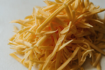 Close up of freshly shredded cheddar cheese on white cutting board