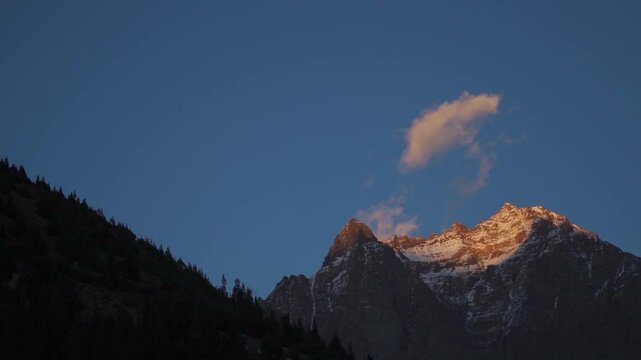 Orange clouds above the snowy Himalayan mountain peak during the sunset as seen from Jispa Village in Lahaul and Spiti district, Himachal Pradesh, India. Orange cloud against the blue sky background.