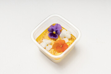 A top-down view of a gourmet dessert, showcasing an elegant presentation with edible flowers and a creamy custard layer in a clear plastic container.