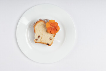 A top-down view of a slice of raisin cake with an orange edible flower, placed on a white plate.