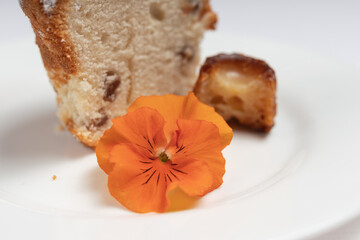 A macro shot of an orange edible flower placed beside a slice of raisin cake with a caramelized pastry.