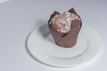 A side-angle view of a traditional kulich bread wrapped in brown paper, sitting on a white plate.