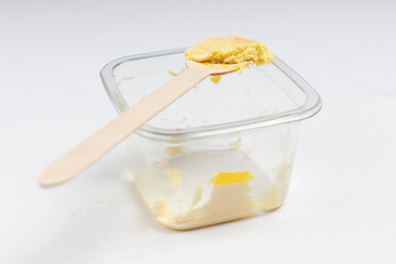 A plastic container with traces of mango dessert and a wooden spoon with a small portion left.