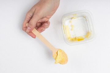 A person holding a wooden spoon with the last bite of mango dessert over an almost empty plastic container.