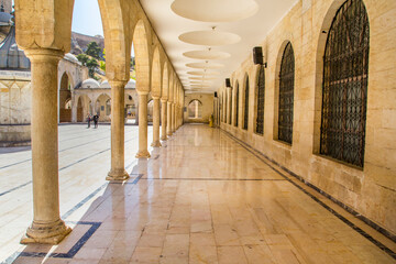 Sanliurfa Urfa Happy Friday A sunlit colonnaded walkway within a historical mosque. A long,...