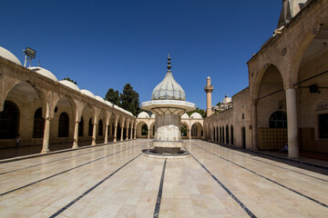 Fototapeta premium Sanliurfa Urfa Turkiye Turkey Tranquil Courtyard of a Historic Mosque in Middle East. A serene courtyard within historical mosque showcasing intricate architectural details and a beautiful fountain