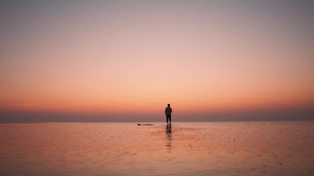 Silhouette shot of an Indian man walk on the water of the Rann of Kutch lake during the sunset at Dholavira in Kutch, Gujarat, India. Man walks on shallow water of the Rann of Kutch lake at sunset.
