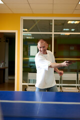 Fototapeta premium A man in a white T-shirt enjoys playing table tennis. Friendly compete in ping pong club