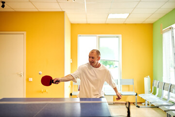 A man in a white T-shirt enjoys playing table tennis. Friendly compete in ping pong club