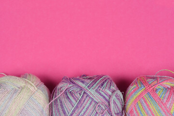 A top-down shot of three colorful yarn balls against a bright pink background, showcasing their variegated patterns and textures
