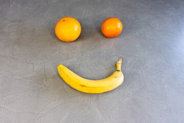 Banana and oranges arranged to form a smiley face on a gray surface