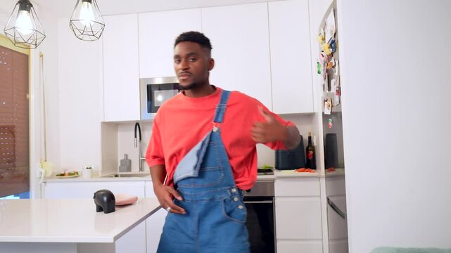 Young man performing dynamic urban dance moves in modern kitchen, expressing joy through rhythmic freestyle movement and creative body language