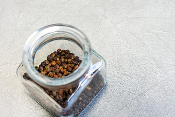 Open spice jar with black peppercorns on a gray countertop