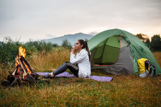 Young brunette sits near a tent and camfire. Enjoys mountain views.