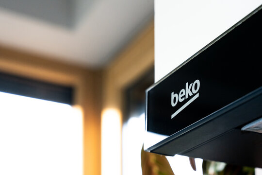 Close-up of Beko kitchen appliance logo with blurred modern interior. Branding and home appliance industry.
