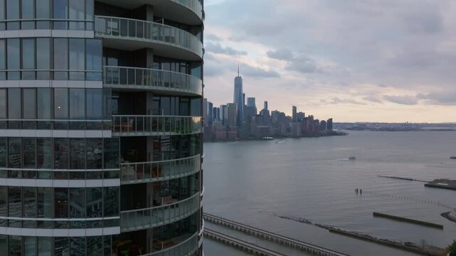 Manhattan skyline revealing One World Trade Center glowing against twilight backdrop, modern residential building in Jersey City in the foreground