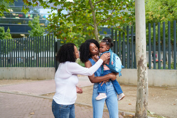 Mother comforting crying toddler daughter next to grandmother in front of school