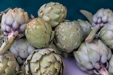Obraz premium Fresh green artichokes with natural textures and subtle purple tones at a market. Perfect for food photography, organic produce, healthy eating, and Mediterranean cuisine concepts