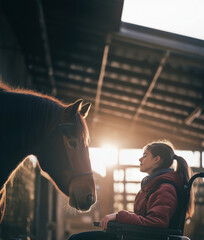 Teenage girl in wheelchair and bay horse in stable looking at each other