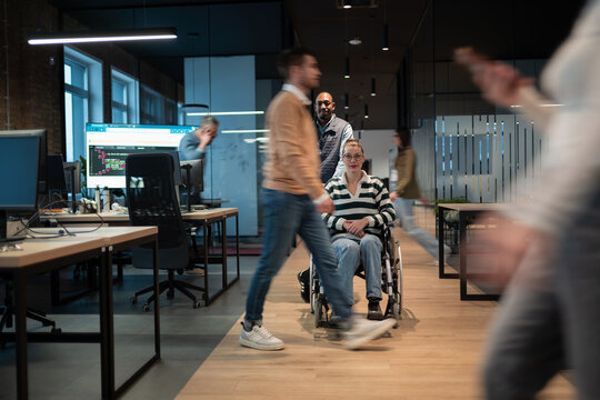 Wheelchair accessibility and inclusion in a startup open space office. A man assists a colleague in a wheelchair while others collaborate, business people, teamwork, innovation and diversity concept