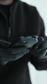 A scammer in black gloves enters a PIN code on the phone.
A man is trying to unlock his mobile phone.
Thief with a phone in his hands.
Black latex gloves and a phone in hands, close-up