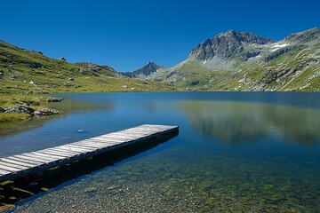 A serene alpine lake with a wooden pier extending into the still water under a clear blue sky