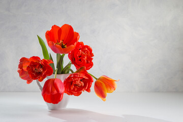 A bouquet of red tulips in a white vase on a light background. Copy space