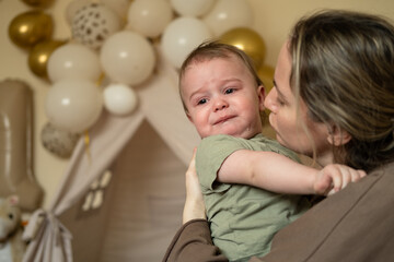 Portrait of a crying baby boy. The child is teething, he is naughty and asks for his mother hands. Mom is calming the baby.