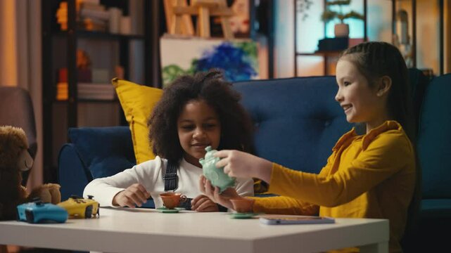 Cheerful multiethnic little girls playing a tea party game, enjoying childhood