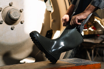 Farmer wearing rubber boots in a garage near tractor wheel