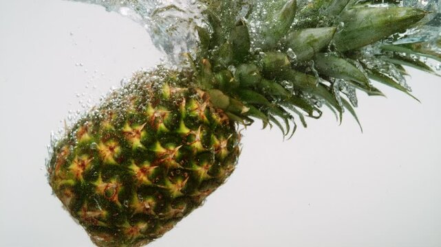 single pineapple or ananas submerging in water on white background in slow motion