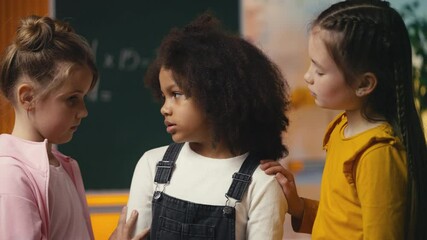 Two caring little girls support and hug their upset classmate, true friendship