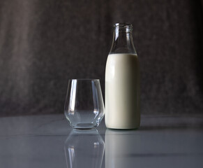 An empty glass is on the table next to a full bottle of milk.
