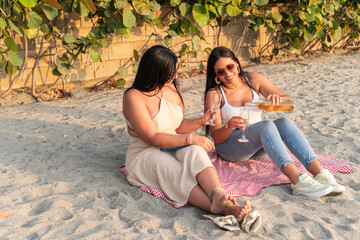 Two women having picnic, drinking white wine at beach