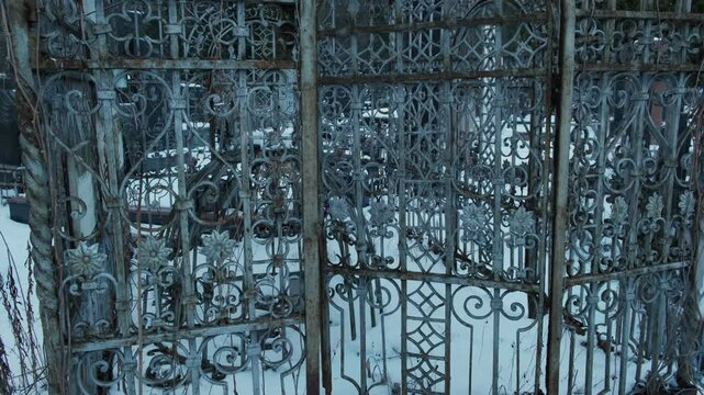 Rusty ornate wrought iron cemetery gate covered in snow, with intricate floral and geometric patterns, evoking a sense of decay, abandonment, and historical mystery