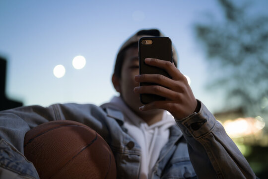 ブルーアワーの夕方にバスケットボールを持ってsns投稿や写真を撮る男の子