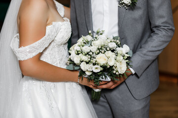 Newlyweds holding hands. The groom is wearing a gray suit with a white shirt, and the bride is...