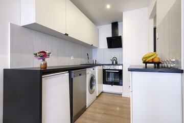 Kuchnia w nowoczesnym apartamencie w jasnym kolorze  z czarnym blatem,  owoce