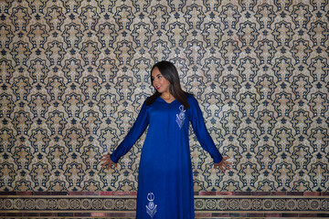 Moroccan woman, young, beautiful, brunette, with blue abaya, standing, smiling and happy leaning...