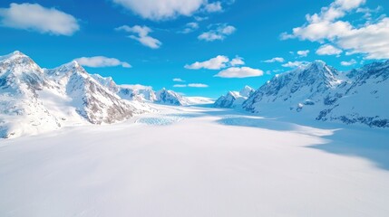 Obraz premium Vast snow-covered glacier valley stretches between rugged mountain peaks under a bright blue sky.