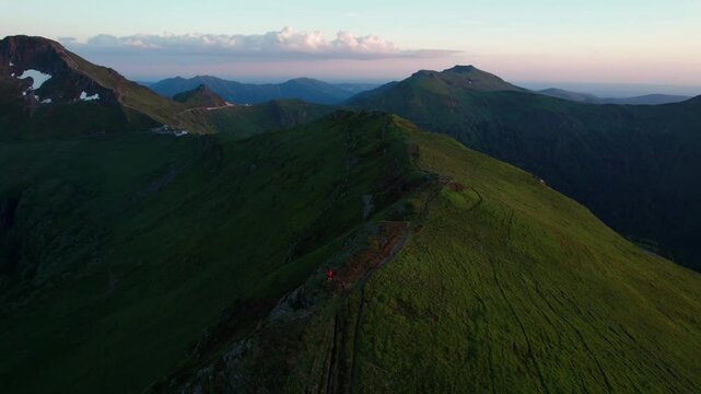 aerial shot revealing Puy Mary Volcano from Puy de la Tourte viewpoint at sunset with a person in red jacket admiring the landscape, Cantal departement, Auvergne Rhone Alpes region, France