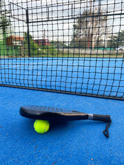 Padel racket and yellow tennis ball on blue turf court outdoors. Popular racquet sport, social game concepts