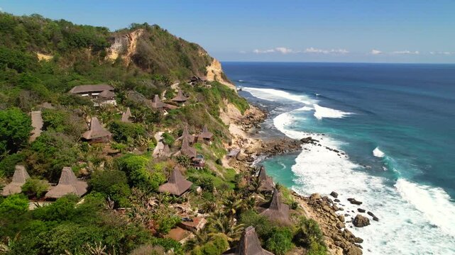 Aerial orbit around traditional thatched-roof villas and pristine beach along coastline at Lelewatu Resort on Sumba Island, Indonesia